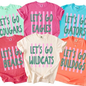 May include: Six short-sleeved crew neck t-shirts in mint, pink, light blue, red, cream, and orange. Each shirt features vertical pink stripes and green text reading Let's Go followed by team names: Cougars, Eagles, Gators, Bears, Wildcats, and Bulldogs.