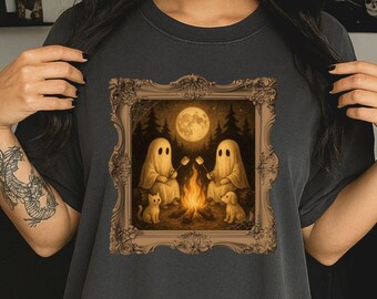 May include: Black t-shirt featuring a framed illustration of two ghosts roasting marshmallows over a campfire under a full moon. A cat and a dog are also in the image. The text "BLACK" is printed on the lower right.