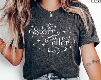Puede incluir: Una camiseta de color gris oscuro jaspeado con el texto "Story Teller" en letras blancas cursivas y pequeñas estrellas blancas. La camiseta la lleva puesta una persona con vaqueros azules y zapatillas blancas.