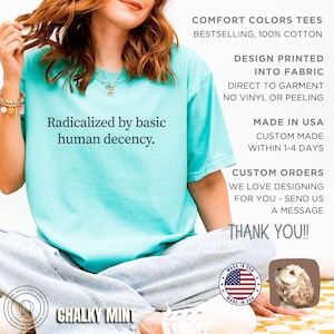 May include: A mint green t-shirt with the phrase "Radicalized by basic human decency" printed in black. The shirt is made of 100% cotton and is part of the Comfort Colors collection. The design is printed directly into the fabric.
