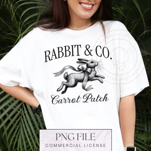 Pode incluir: Camiseta branca com uma ilustração em preto e branco de um coelho com um laço e o texto "RABBIT & CO. Carrot Patch" impresso nela.