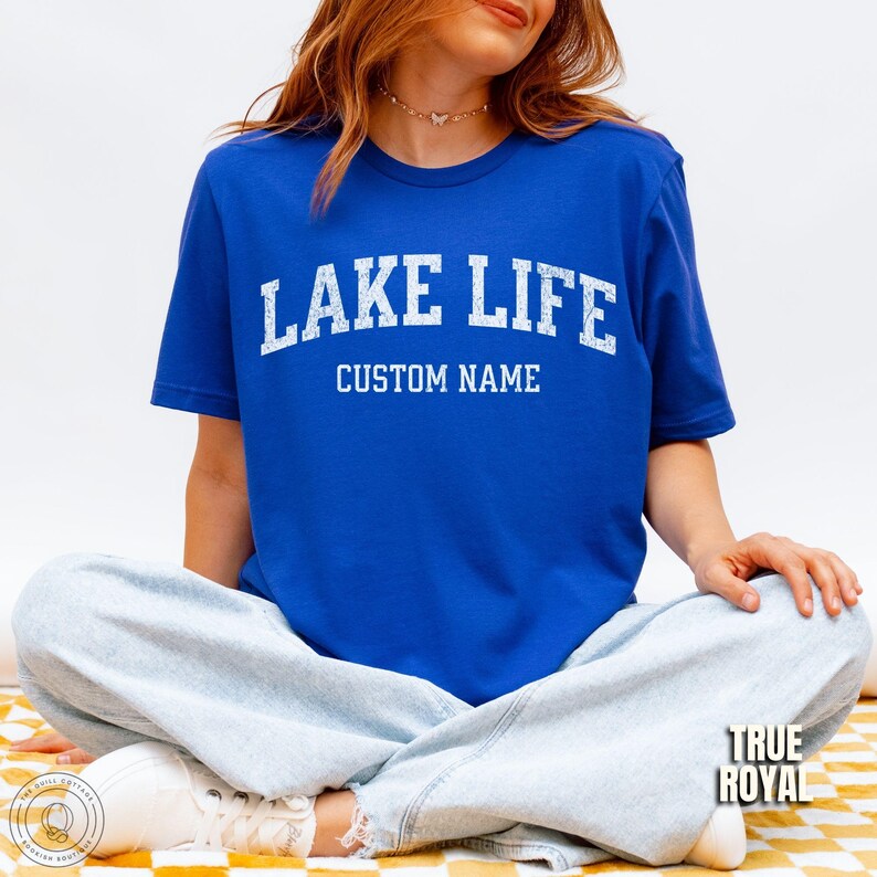 Peut inclure: T-shirt bleu roi avec l'inscription "LAKE LIFE" en lettres blanches au-dessus de "CUSTOM NAME". Le t-shirt est &agrave; manches courtes et a un col rond. L'image montre &eacute;galement un jean bleu clair.
