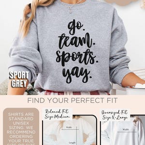 May include: A gray sweatshirt with the text 'go team. sports. yay.' in black. The sweatshirt is shown on a model. The text 'Sport Grey' is shown in the lower left corner of the image. The text 'Cozy Soft' is shown in the upper right corner of the image. The text 'Find Your Perfect Fit' is shown in the center of the image. The image shows two different sizes of the sweatshirt: a relaxed fit size medium and an oversized fit size x-large. The image shows the width and length of each size.