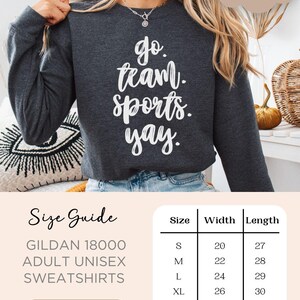 May include: A dark heather gray sweatshirt with the text 'go team. sports. yay.' in white. The sweatshirt is a Gildan 18000 adult unisex sweatshirt. A size chart is shown with the sizes S, M, L, XL, 2XL, and 3XL, and the corresponding width and length measurements in inches.