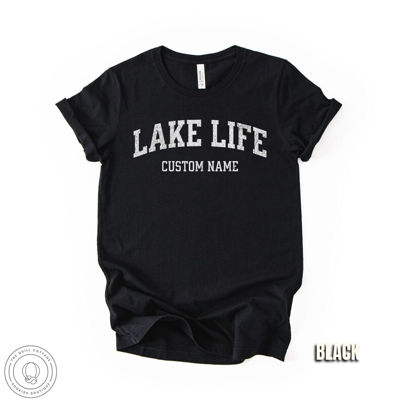Peut inclure: T-shirt noir avec l'inscription "LAKE LIFE" au-dessus de "CUSTOM NAME" en lettres blanches et us&eacute;es. Le t-shirt a des manches retrouss&eacute;es et un col rond. Le mot "BLACK" est dans le coin inf&eacute;rieur droit.
