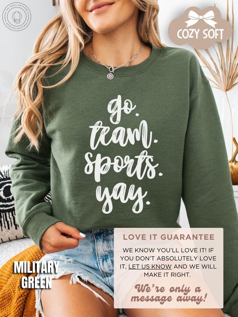 May include: A green sweatshirt with the text 'go team sports yay.' printed in white. The sweatshirt is displayed on a model wearing denim shorts. The text 'COZY SOFT' is in a pink cloud shape in the upper right corner of the image. The text 'MILITARY GREEN' is in the lower left corner of the image. The text 'LOVE IT GUARANTEE' is in a pink rectangle in the lower right corner of the image. The text 'WE KNOW YOU'LL LOVE IT! IF YOU DON'T ABSOLUTELY LOVE IT, LET US KNOW AND WE WILL MAKE IT RIGHT. We're only a message away!' is in the pink rectangle below the text 'LOVE IT GUARANTEE'.
