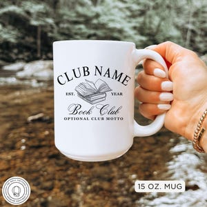 May include: White ceramic mug with the text "CLUB NAME" above a stack of books and the words "Book Club". The mug also has the text "EST. YEAR" and "OPTIONAL CLUB MOTTO". The mug is 15 oz.