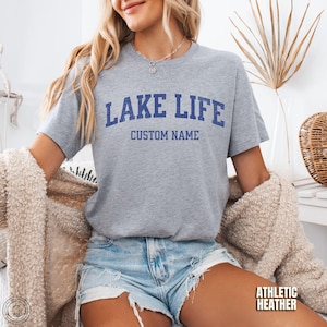 Peut inclure: Un t-shirt gris chin&eacute; avec les mots "LAKE LIFE" en lettres bleues. En dessous, la phrase "CUSTOM NAME" est &eacute;galement en bleu. Le t-shirt est &agrave; manches courtes et en mati&egrave;re athletic heather.