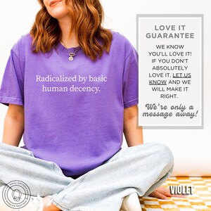 May include: A violet t-shirt with the text "Radicalized by basic human decency" in white. The image also includes a "Love It Guarantee" and the text "We're only a message away!"