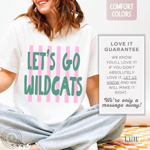 May include: A white short-sleeve t-shirt featuring vertical pink stripes and the green text "LET'S GO WILDCATS" printed on the front. The shirt is paired with light blue denim jeans. A text box on the right displays "LOVE IT GUARANTEE".