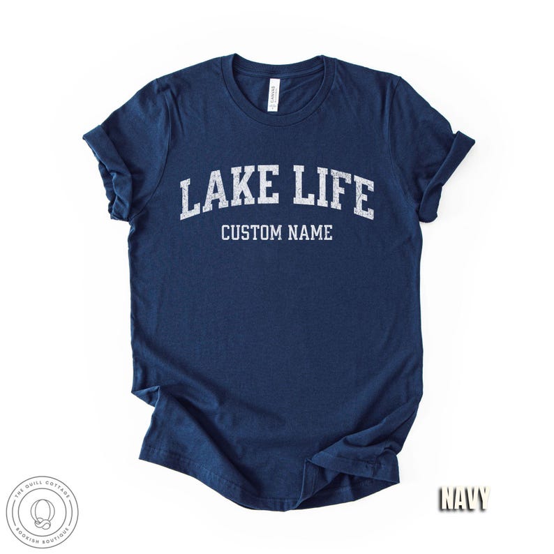 Peut inclure: T-shirt bleu marine avec l'inscription blanche "LAKE LIFE" en arc au-dessus de "CUSTOM NAME". Les manches sont retrouss&eacute;es. Le mot "NAVY" est imprim&eacute; en bas &agrave; droite. Le t-shirt a une &eacute;tiquette au niveau de l'encolure.