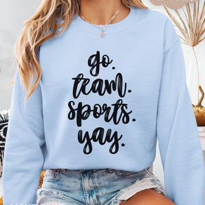 May include: A light blue sweatshirt with the text 'go team sports yay' in black lettering.