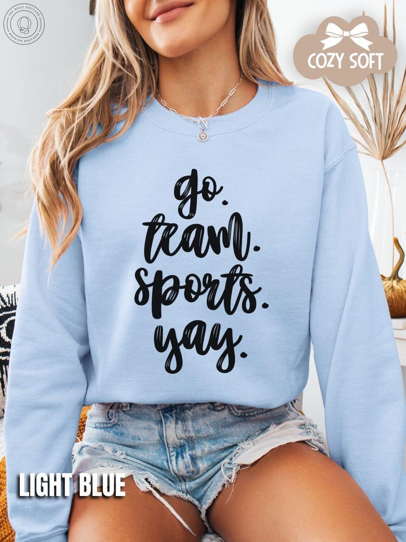 May include: A light blue sweatshirt with the text 'go team sports yay' in black lettering.