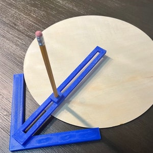 May include: A blue plastic circle-drawing tool with a pencil inserted through the center. The tool is positioned on a round piece of wood.