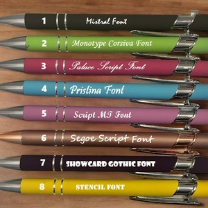 May include: Eight pens with different colored bodies and silver accents. Each pen has a number and a font name printed on it. The font names are: Mistral Font, Monotype Corsiva Font, Palace Script Font, Pristina Font, Script MT Font, Segoe Script Font, SHOWCARD GOTHIC FONT, STENCIL FONT.