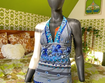 May include: A vintage halter top with a blue floral pattern on a gray background. The top features a halter neck and a fitted bodice. The design includes blue flowers and stripes. The top is displayed on a mannequin.