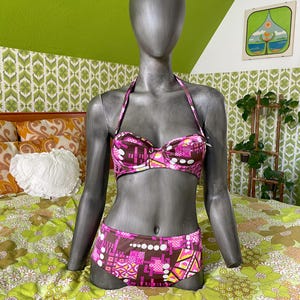 May include: A two-piece bikini set in a retro style, displayed on a mannequin. The top and bottom feature a geometric pattern in shades of pink, brown, yellow, and white. The halter top has a sweetheart neckline.
