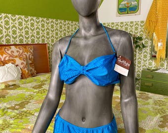 May include: A blue bikini set with a bow-shaped top and matching bottoms. The swimsuit is displayed on a mannequin. The bikini has a striped pattern. A tag with the text "Rene Philip" is attached to the bikini.