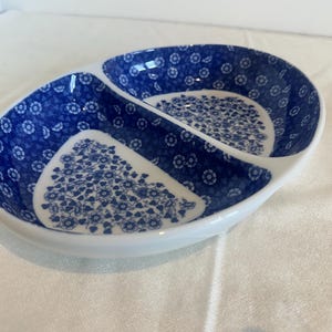 May include: Oval serving dish with two compartments, featuring a white base and a blue floral pattern. The dish is divided into two sections, each with a different floral design. The rim is white, and the design is classic and elegant.