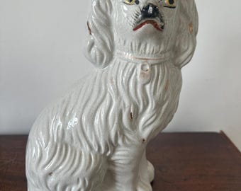 May include: A white ceramic figurine of a dog with black painted eyes and a red painted mouth. The dog is sitting with its head tilted up and its ears perked.