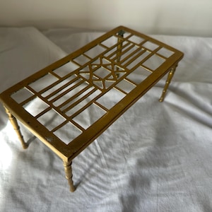 May include: A rectangular gold-toned metal table with a lattice-style openwork top featuring a central geometric star pattern. The table is supported by four slender, segmented legs that resemble bamboo stalks, providing a stable base.