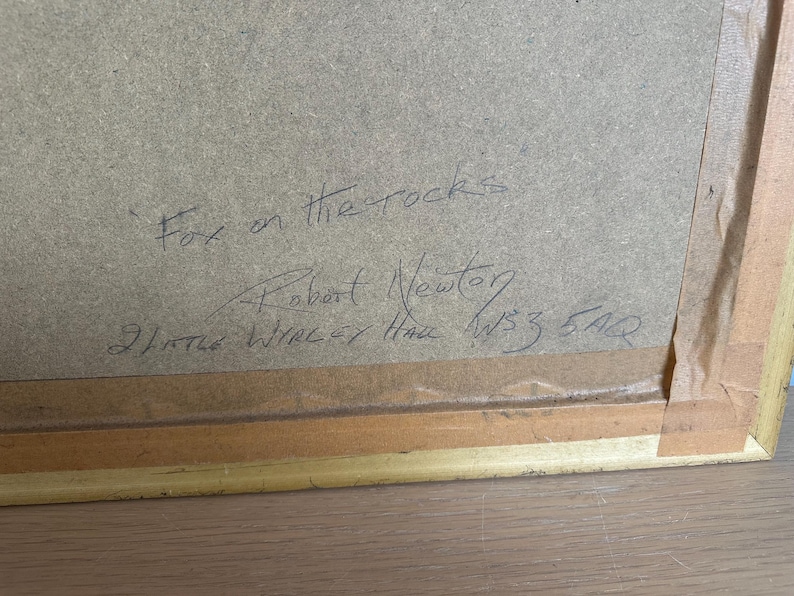 May include: A framed artwork with the title "Fox on the rocks" handwritten in black ink. The artist's name, Robert Newton, and address are also visible. The frame is gold-colored.