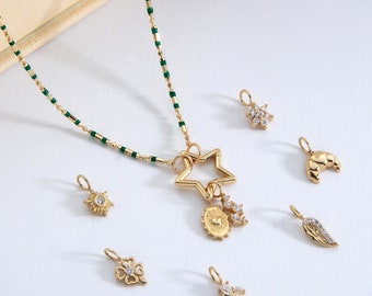 Puede incluir: Un collar de oro con una cadena de cuentas verdes y un dije de estrella con dijes más pequeños unidos. El collar se muestra con varios otros dijes, incluyendo una flor, una luna creciente, un sol, una hoja y un racimo de cristales.