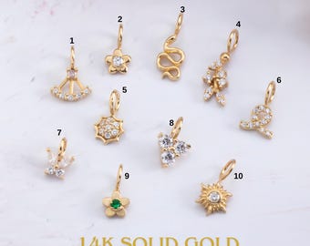 Puede incluir: Una colección de diez colgantes de oro macizo de 14K con varios diseños, incluyendo un abanico, una flor, una serpiente, una figura, una estrella, un lazo, una corona, un corazón y un sol. Cada colgante está adornado con gemas transparentes.