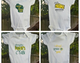 May include: Four white baby onesies with green and yellow text and graphics. One says "Cutest Lil' Cheese Curd" with a Wisconsin outline. Another says "Little Cheesehead (in training)". The third says "Itty Bitty Packer's FAN". The last says "I drool green & gold".