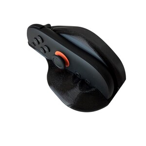 May include: A black gaming controller with an orange accent button is inserted into a black, textured grip. The controller has several buttons and a joystick. The grip appears to be 3D-printed.