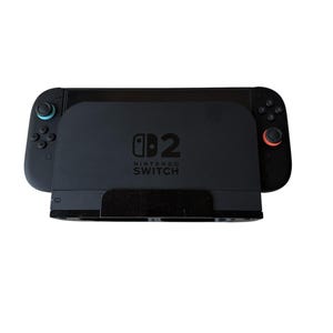 May include: A black Nintendo Switch console with attached controllers. The console is docked in a black charging station. The controllers have blue and red accents. The Nintendo Switch logo is visible on the console.