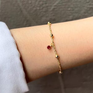 May include: A gold chain bracelet with small round beads and a dangling red gemstone charm.