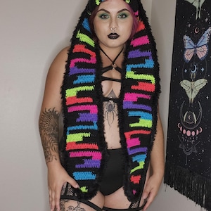 May include: A black crochet hooded scarf with colorful stripes of pink, green, blue, and yellow. The scarf has a fuzzy black trim.
