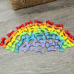 May include: A rainbow assortment of small, white polka dot bows made of ribbon. The bows are arranged in a semi-circle on a wood surface.