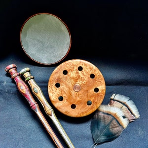 Puede incluir: Dos clavijas de madera con pintura colorida y una base de madera y metal con agujeros. También hay un objeto redondo gris y una pluma de pavo marrón y negro en la imagen.