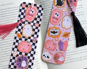 May include: Two decorative bookmarks with Halloween-themed designs. One features a black and white checkered pattern with a pink tassel, the other a light purple background with a black tassel. Both have ghost, pumpkin, and spiderweb illustrations.
