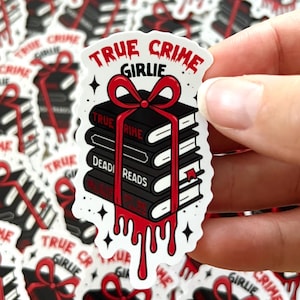 Op de afbeelding: Een witte sticker met de tekst "TRUE CRIME GIRLIE" bovenop een stapel zwarte boeken, vastgebonden met een rode strik en druipend rood bloed. De boeken hebben de woorden "TRUE CRIME" en "DEAD READS" op de ruggen.