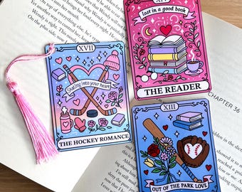 May include: Four colorful bookmarks with romantic themes. One says "lost in a good book", another "The Reader", a third "The Hockey Romance", and the last "Out of the Park Love". Each bookmark has a tassel.