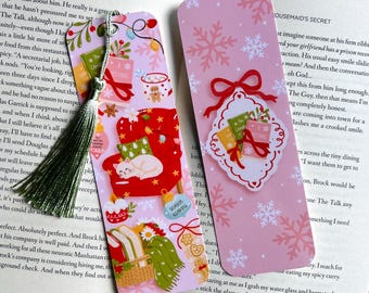 May include: Two decorative bookmarks with Christmas-themed illustrations. One features a red armchair with a sleeping cat, gifts, and ornaments. The other has snowflakes and a gift tag. Both have tassels and are on a book.