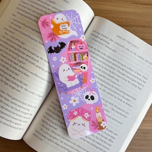 May include: A whimsical bookmark with a lavender background, featuring cartoon ghosts, bats, and a skull. The bookmark has a bookshelf, a mushroom, and a candle design. The text "Potion Recipes" is visible on the bookmark.