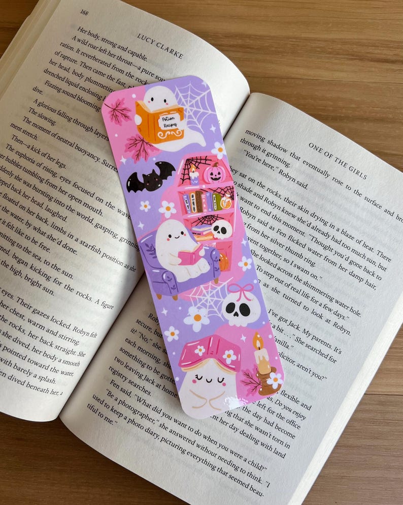 May include: A whimsical bookmark with a lavender background, featuring cartoon ghosts, bats, and a skull. The bookmark has a bookshelf, a mushroom, and a candle design. The text "Potion Recipes" is visible on the bookmark.