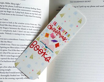 May include: A white bookmark with the text "ALL I WANT FOR CHRISTMAS IS MORE BOOKS" in red and blue. The bookmark features illustrations of books, snowflakes, and Christmas trees. It is placed inside an open book.