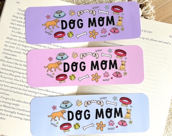 May include: Three rectangular bookmarks with a dog theme. Each bookmark has the words "DOG MOM" in large black letters, along with dog-related illustrations. The bookmarks are in pastel purple, pink, and blue.