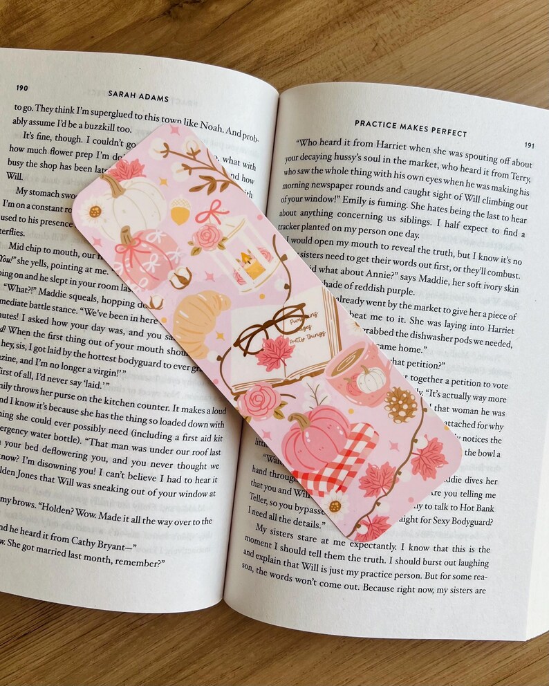 Op de afbeelding: Een roze en witte bladwijzer met herfstthema, met pompoenen, bladeren en een croissant. De bladwijzer is rechthoekig met afgeronde hoeken en ligt op een open boek.