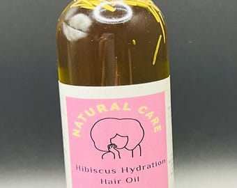 May include: A clear glass bottle with a black cap and a dropper top. The bottle is filled with a yellow liquid and contains herbs. The label reads "Natural Care Hibiscus Hydration Hair Oil All Natural Ingredients Made in the USA".