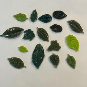 May include: Assortment of green and light green resin leaves, some with a textured surface, for crafting or decorative purposes.