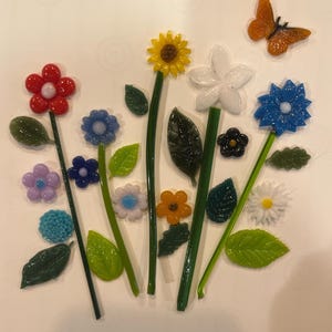 May include: A collection of colorful glass flowers and leaves, along with an orange butterfly. The flowers are in various colors, including red, blue, yellow, white, and purple. The leaves are green, and the butterfly has orange and brown details.