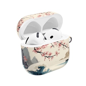 May include: A white wireless earbud charging case with an open lid, containing two white earbuds. The exterior of the case features a printed design of pink cherry blossoms on branches, grey mountains, and a stylized blue ocean wave.