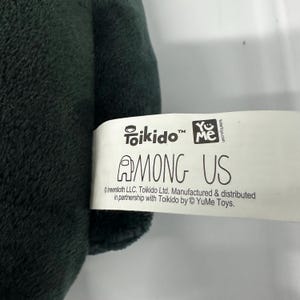 以下が含まれることがあります： 白いタグが付いた濃い緑色のぬいぐるみ。タグには「Toikido」と「AMONG US」の文字が記載されています。タグには「Innersloth LLC. Toikido Ltd. Manufactured & distributed in partnership with Toikido by YuMe Toys.」の文字も含まれています。