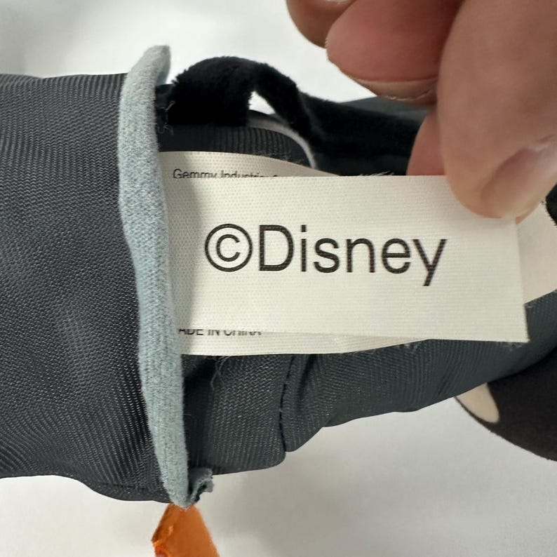 以下が含まれることがあります： 黒とグレーの体をしたぬいぐるみ。 「&copy;Disney」のロゴが入った白いタグが見えます。 おもちゃは人の手で持たれています。